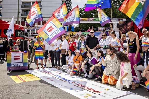 Auf dem Bild sind etwa zwanzig Menschen zu sehen, die hinter einem Banner stehen, auf dem "Vielfalt, Offenheit, Toleranz" steht. Einige haben Regenbogenfahnen mit dem Logo des Paritätischen in der Hand.